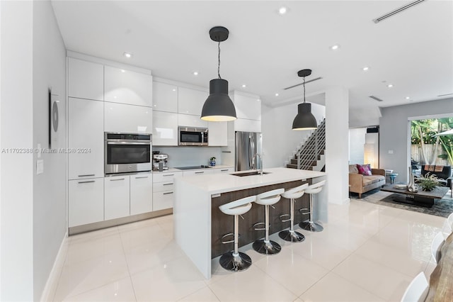 kitchen with a kitchen island with sink, light tile patterned floors, decorative light fixtures, white cabinetry, and stainless steel appliances