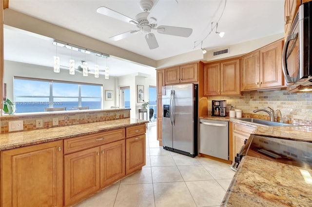 kitchen with light stone countertops, sink, stainless steel appliances, decorative light fixtures, and a water view