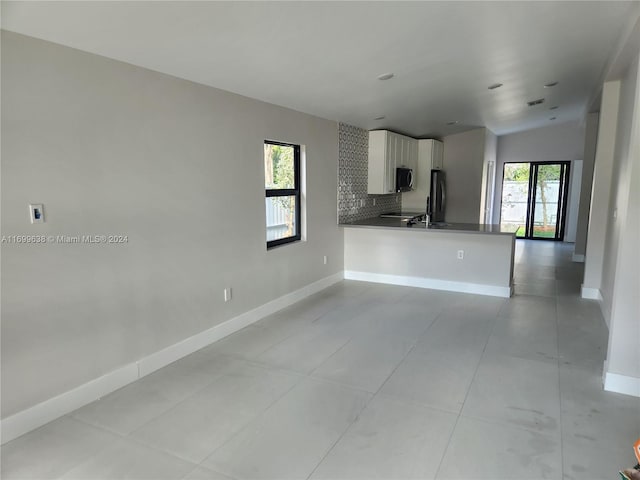 kitchen featuring white cabinets, refrigerator, vaulted ceiling, decorative backsplash, and kitchen peninsula