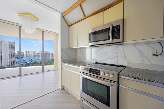 kitchen featuring appliances with stainless steel finishes, tasteful backsplash, cream cabinets, stone countertops, and light hardwood / wood-style floors