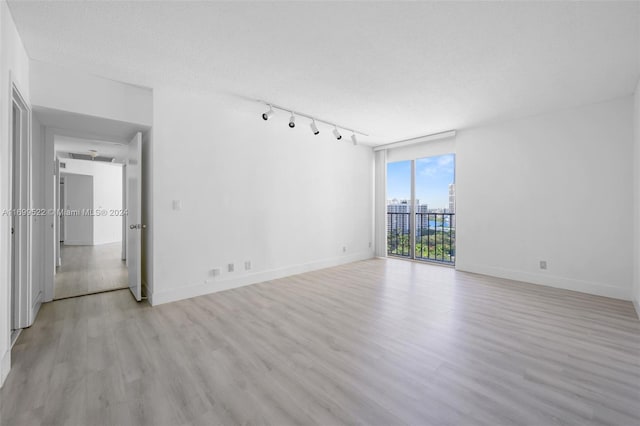 empty room with a wall of windows, a textured ceiling, light hardwood / wood-style floors, and rail lighting