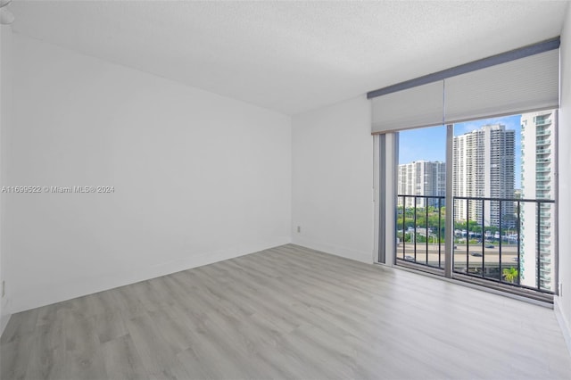 spare room with expansive windows, light wood-type flooring, and a textured ceiling