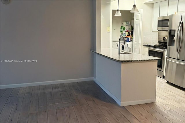 kitchen with kitchen peninsula, appliances with stainless steel finishes, decorative light fixtures, and light hardwood / wood-style flooring