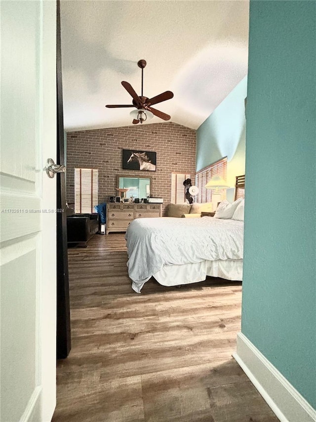 bedroom with hardwood / wood-style flooring, vaulted ceiling, ceiling fan, and brick wall