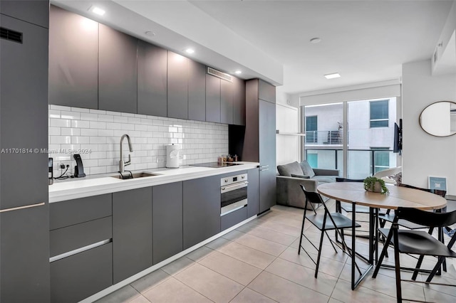 kitchen featuring gray cabinetry, oven, sink, decorative backsplash, and light tile patterned flooring