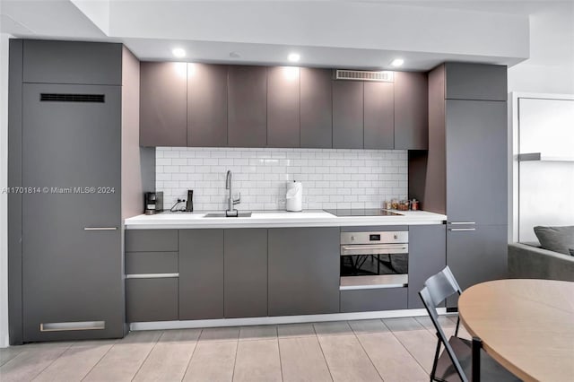 kitchen with stainless steel oven, sink, decorative backsplash, gray cabinets, and black electric cooktop