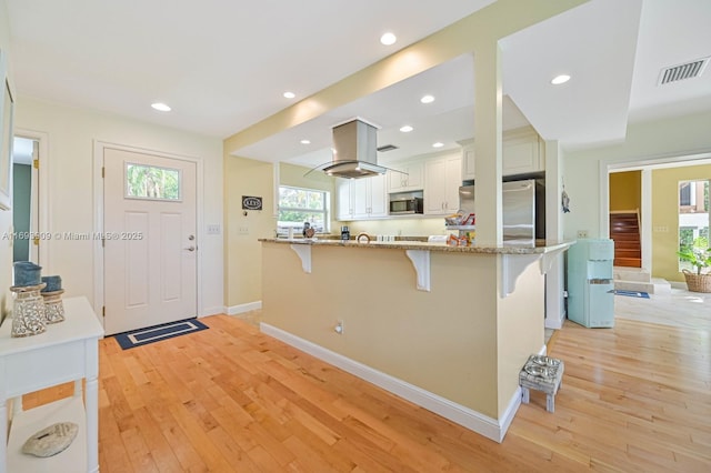 671 Live Oak Ln, La Belle, FL 33935 - kitchen with visible vents, a kitchen bar, white cabinetry, island exhaust hood, and stainless steel appliances
