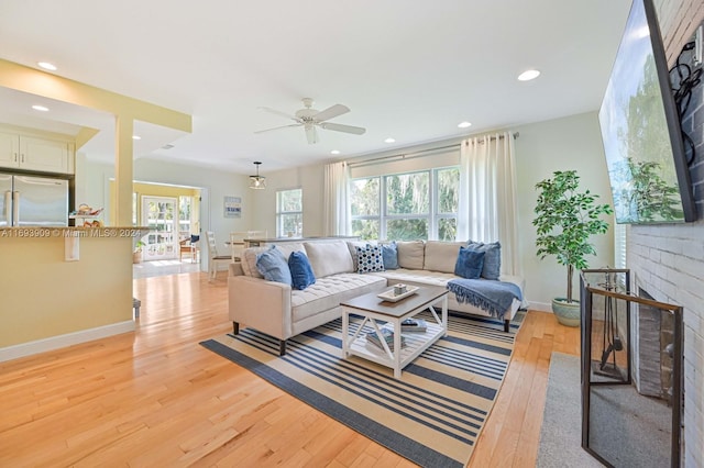 living room with a fireplace, ceiling fan, light hardwood / wood-style flooring, and a healthy amount of sunlight