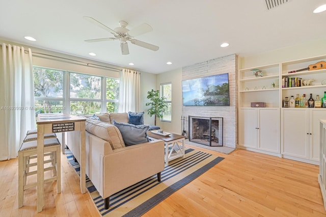 living room featuring ceiling fan, light hardwood / wood-style floors, and a brick fireplace