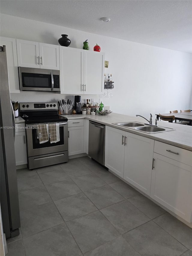 kitchen featuring tile patterned floors, sink, appliances with stainless steel finishes, white cabinetry, and kitchen peninsula