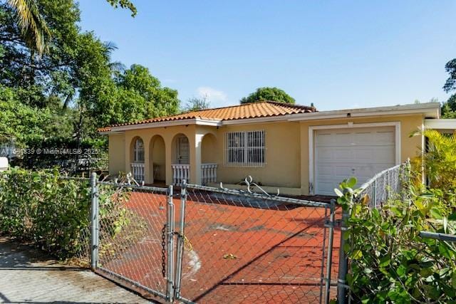 mediterranean / spanish house featuring stucco siding, a gate, a tile roof, a fenced front yard, and an attached garage