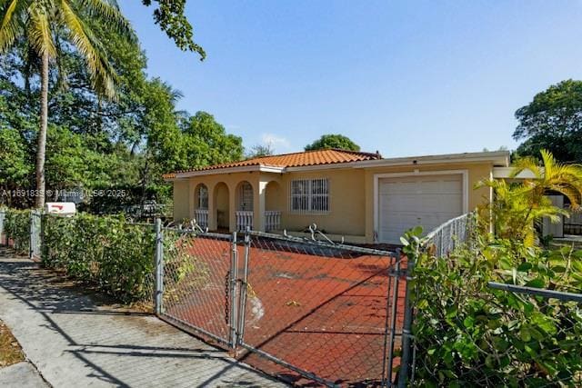 mediterranean / spanish-style house with stucco siding, a gate, a fenced front yard, a garage, and a tiled roof