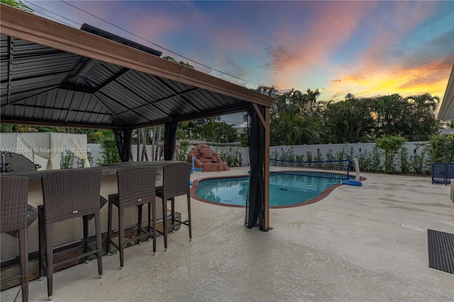 pool at dusk featuring a gazebo, an outdoor bar, and a patio