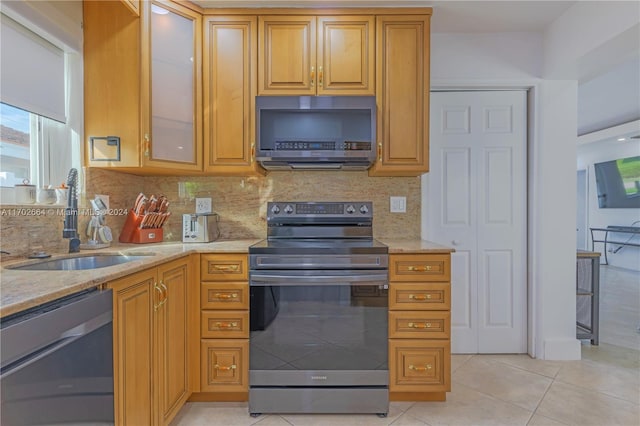 kitchen featuring sink, decorative backsplash, appliances with stainless steel finishes, light tile patterned flooring, and light stone counters