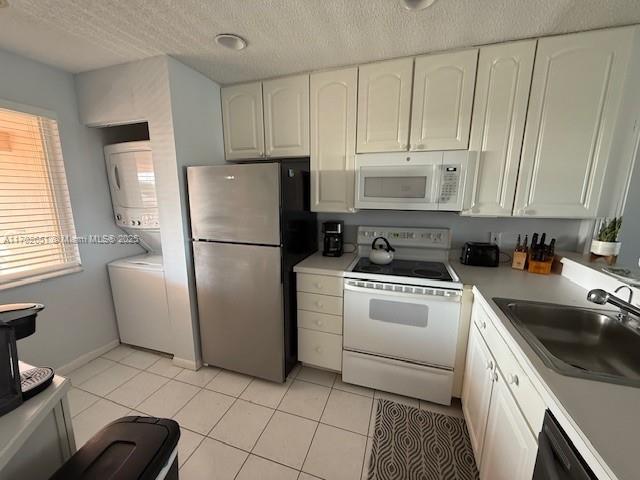 kitchen featuring light tile patterned flooring, white appliances, stacked washer / drying machine, and sink