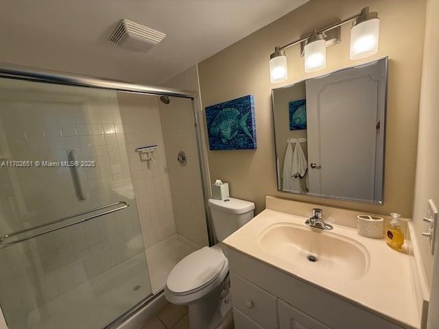 bathroom featuring tile patterned flooring, toilet, vanity, and a shower with shower door