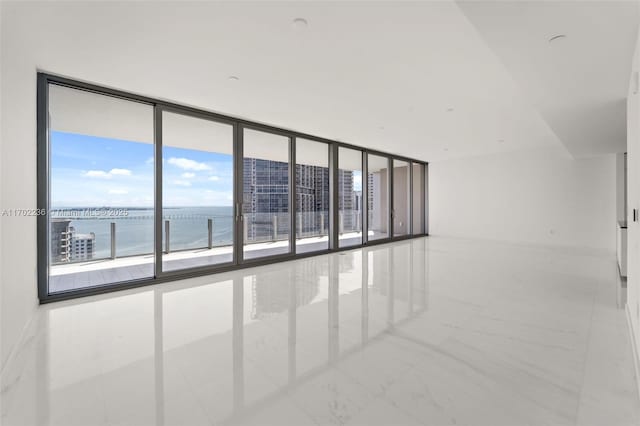 unfurnished room featuring marble finish floor, a wall of windows, and a water view