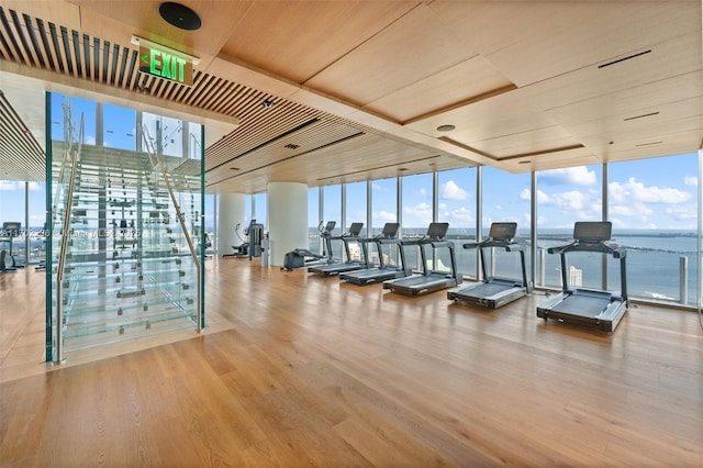 exercise room featuring light wood-style floors, wood ceiling, floor to ceiling windows, and a water view