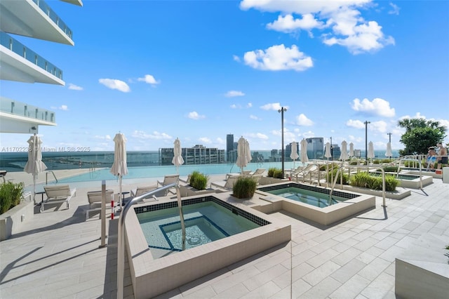 view of swimming pool featuring a community hot tub, a patio area, a city view, and a water view