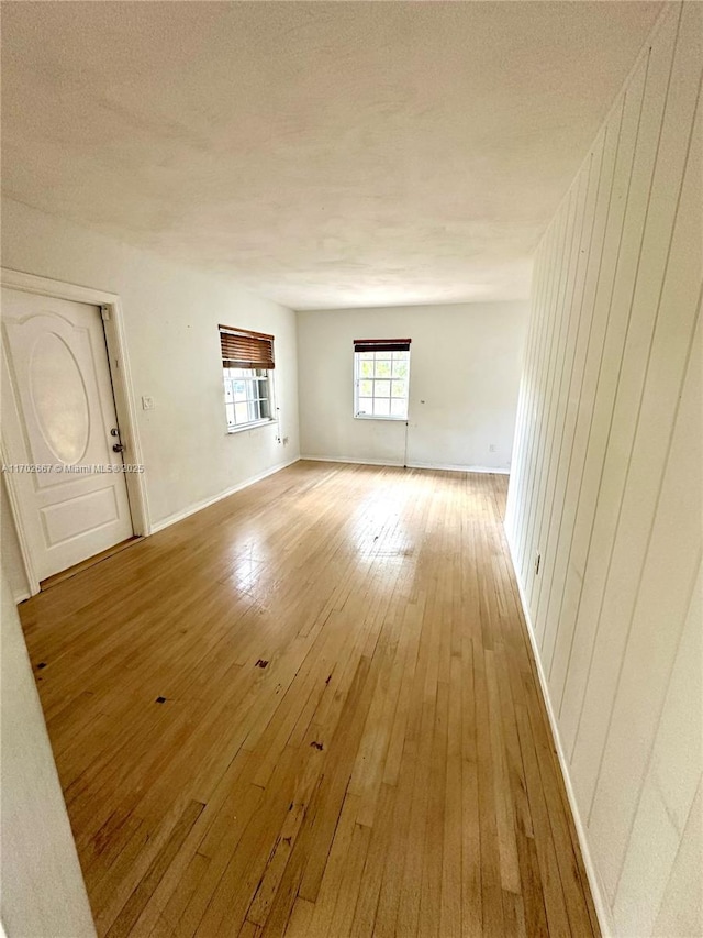 unfurnished living room featuring a textured ceiling, light wood finished floors, and baseboards