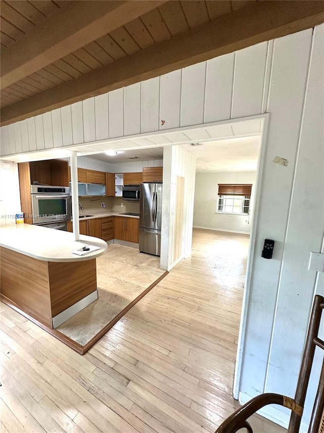 kitchen with brown cabinets, stainless steel appliances, light wood-style flooring, wooden ceiling, and a peninsula