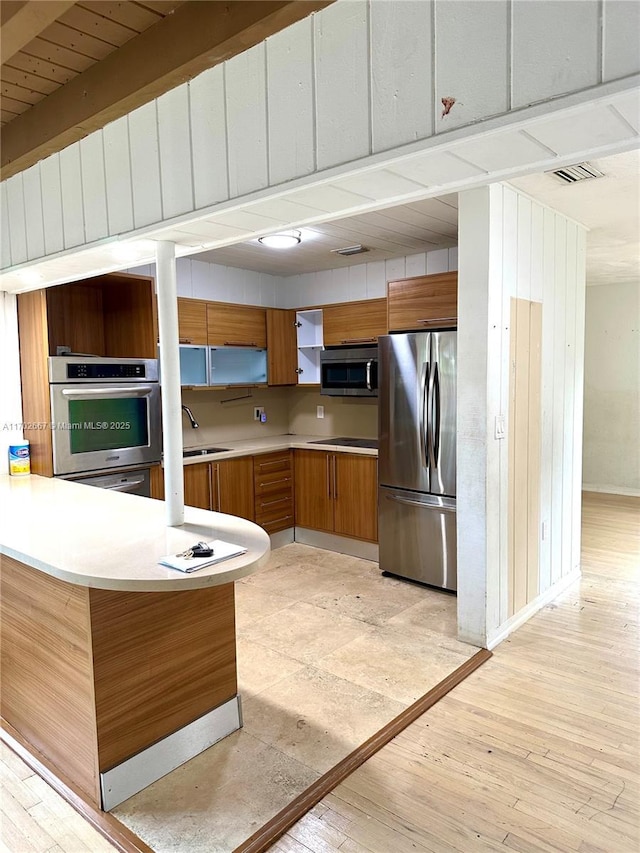 kitchen featuring stainless steel appliances, light countertops, light wood-type flooring, brown cabinets, and open shelves