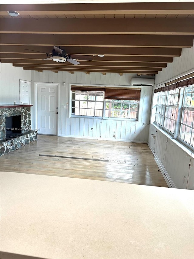 interior space with a ceiling fan, beamed ceiling, a stone fireplace, and a wall mounted AC