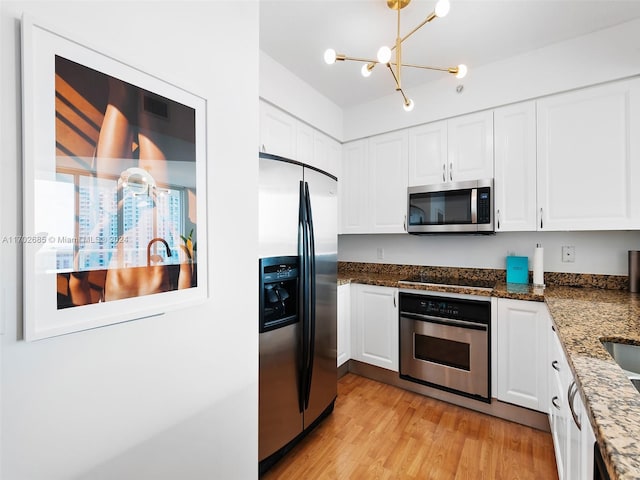 kitchen with a chandelier, appliances with stainless steel finishes, light hardwood / wood-style floors, and white cabinetry