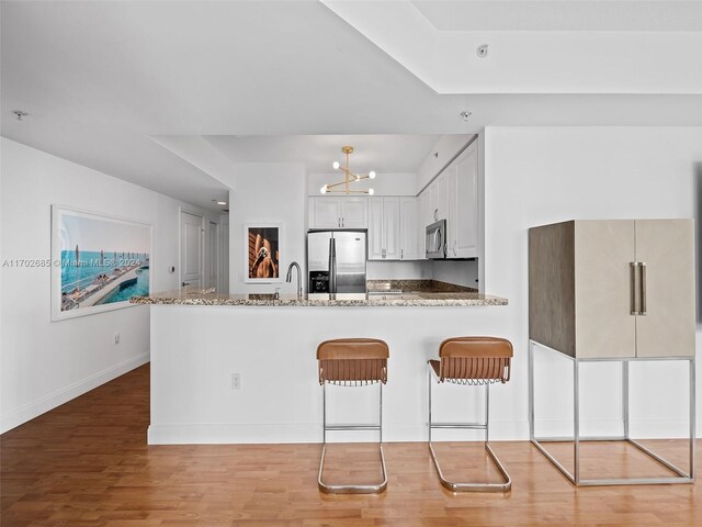 kitchen with white cabinets, dark stone countertops, light wood-type flooring, appliances with stainless steel finishes, and kitchen peninsula