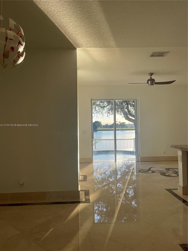 interior space with a textured ceiling, a water view, and ceiling fan