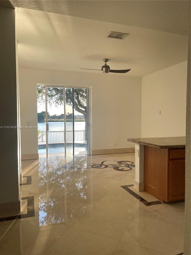 unfurnished room with ceiling fan, a water view, and a textured ceiling