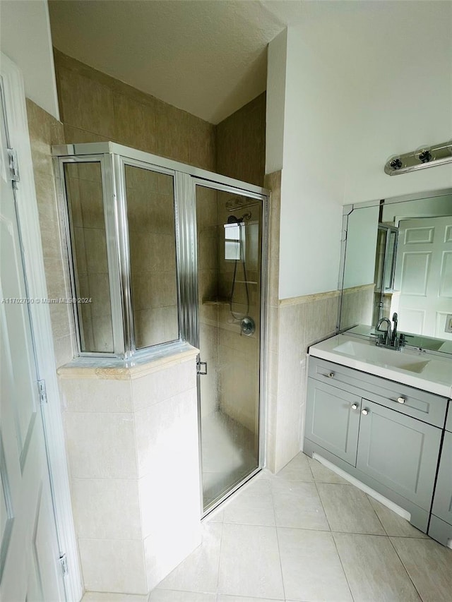 bathroom featuring tile patterned floors, vanity, an enclosed shower, and tile walls