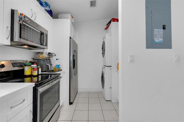 kitchen with electric panel, white cabinets, stacked washer and dryer, light tile patterned flooring, and stainless steel appliances