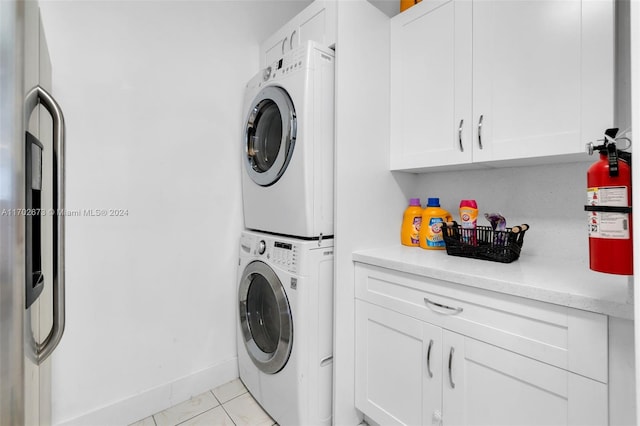 laundry area with light tile patterned flooring, cabinets, and stacked washer and clothes dryer