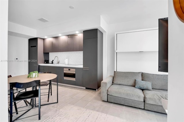 kitchen with decorative backsplash, light tile patterned floors, sink, and stainless steel oven