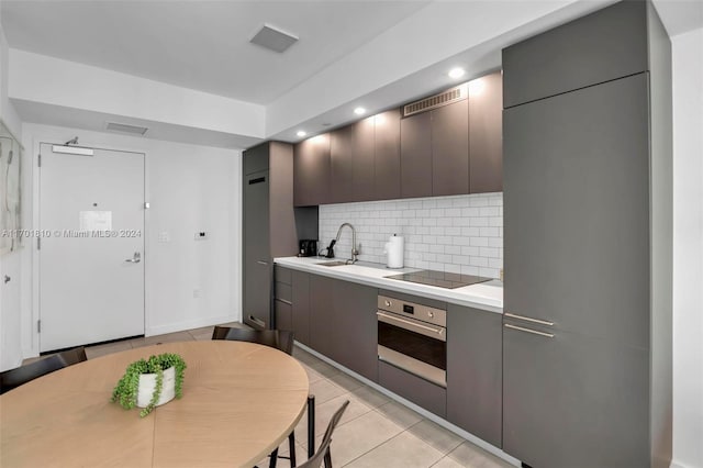 kitchen with sink, tasteful backsplash, oven, black electric stovetop, and light tile patterned floors