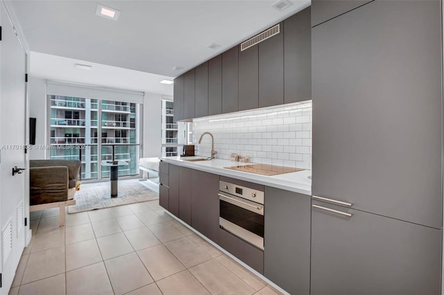 kitchen with stainless steel oven, sink, decorative backsplash, black electric cooktop, and light tile patterned floors