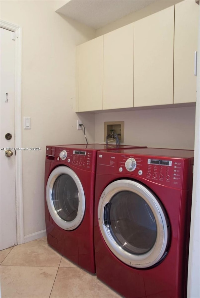 laundry room featuring washing machine and clothes dryer, light tile patterned floors, and cabinets