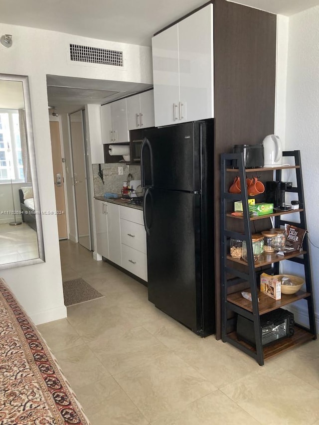 kitchen featuring white cabinets, backsplash, and black fridge