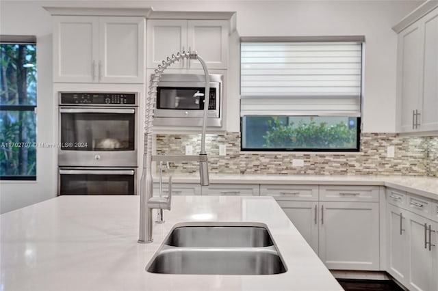 kitchen with appliances with stainless steel finishes, backsplash, white cabinetry, and a wealth of natural light