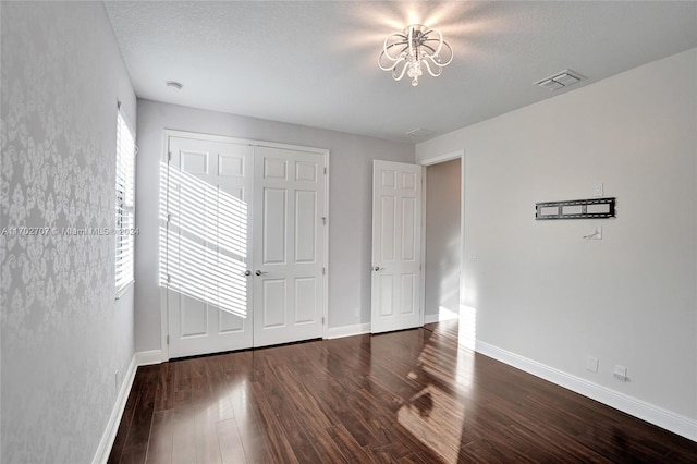 unfurnished bedroom featuring a textured ceiling, a closet, dark hardwood / wood-style floors, and a notable chandelier