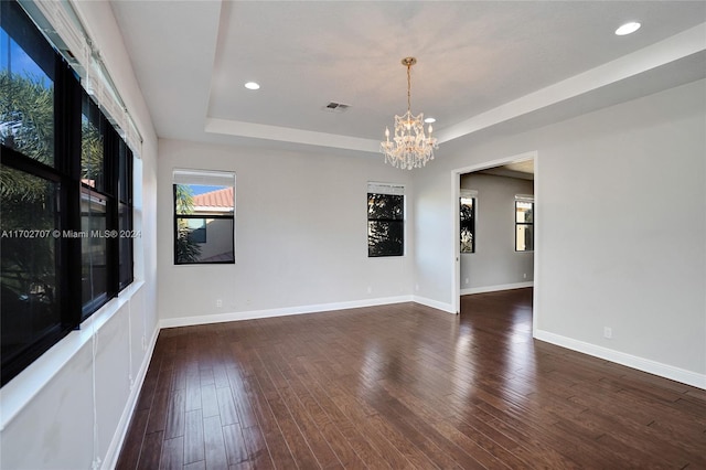 empty room with a tray ceiling, dark hardwood / wood-style floors, and an inviting chandelier