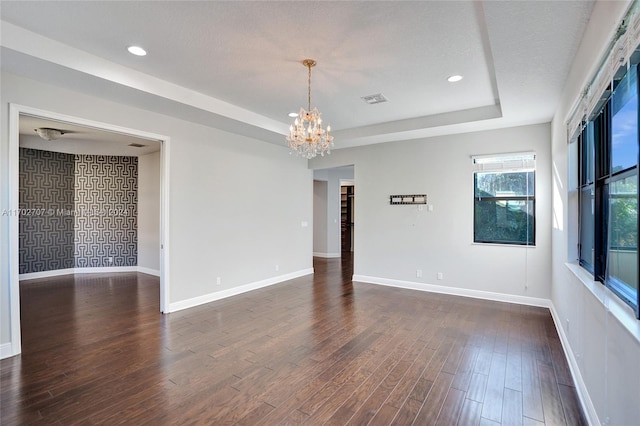 unfurnished room with a tray ceiling, a textured ceiling, dark hardwood / wood-style floors, and an inviting chandelier