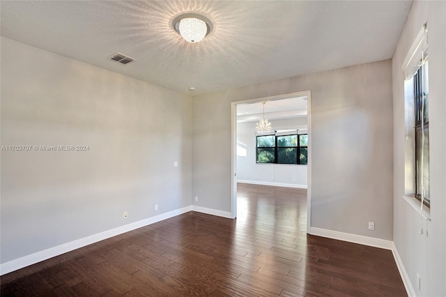 empty room featuring a textured ceiling, dark hardwood / wood-style floors, and an inviting chandelier