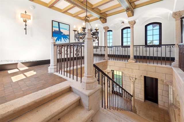 staircase featuring an inviting chandelier, ornate columns, and beamed ceiling