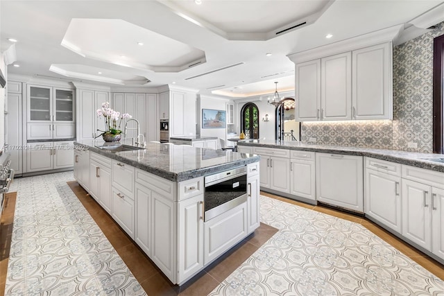 kitchen featuring an island with sink, white cabinets, a tray ceiling, and sink