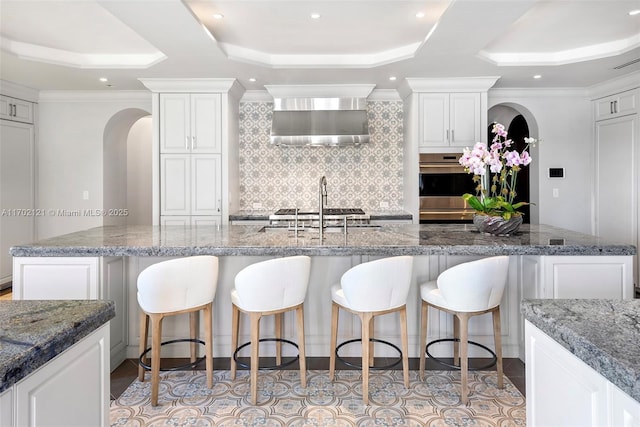 kitchen with white cabinetry, dark stone countertops, a tray ceiling, and a large island