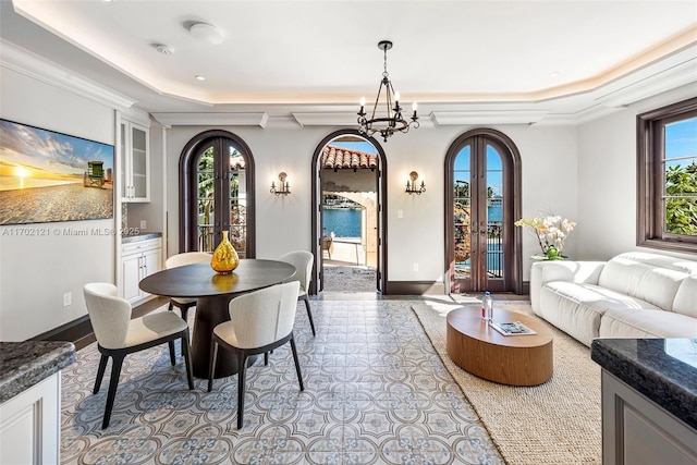 dining space featuring a raised ceiling, french doors, plenty of natural light, and an inviting chandelier