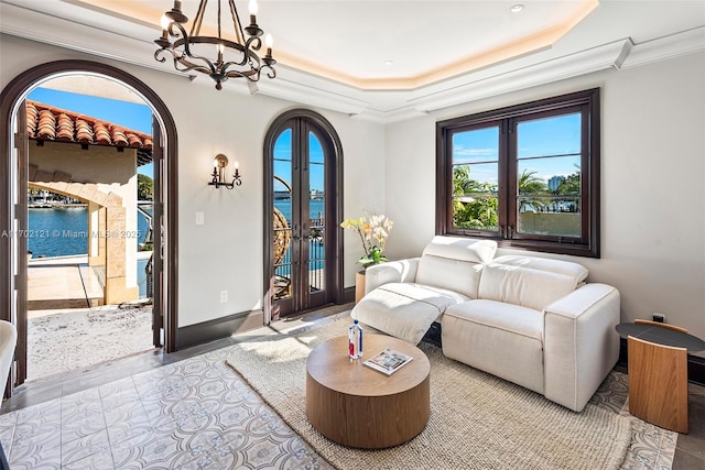 living room with an inviting chandelier, crown molding, a tray ceiling, a water view, and french doors