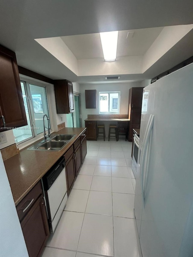 kitchen with dark brown cabinets, white appliances, a raised ceiling, sink, and light tile patterned floors